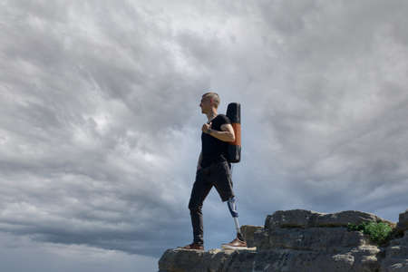 a man on a prosthetic leg travels the mountains. Dressed in black jeans and a T-shirt, he carrying matの写真素材