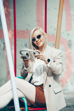 Portrait of blonde woman with headphones in hands. Hipster fashion model wear stylish wireless headphones enjoy listen new cool music.の写真素材