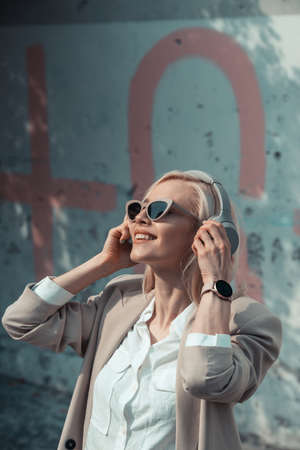 Portrait of blonde woman in headphones listening music with sunglasses. Hipster fashion model wear...
