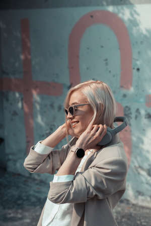 Portrait of blonde woman with headphones in hands. Hipster fashion model wear stylish wireless headphones enjoy listen new cool music.の写真素材