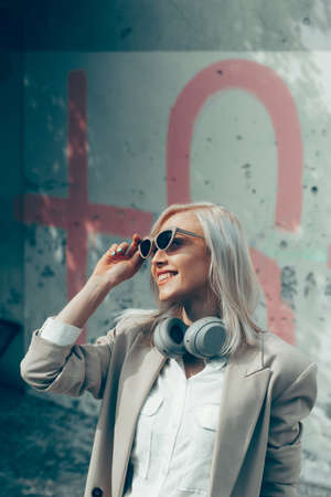 Portrait of blonde woman with headphones in hands. Hipster fashion model wear stylish wireless...
