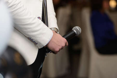 Business and speech topic: Man in a white jacket holding a black microphone. Vertical photoの写真素材