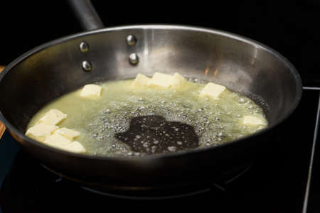 Pieceses of butter melted in a frying pan on a gas stoveの写真素材