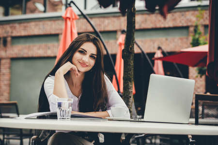 Young freelancer woman using laptop computer sitting at cafe table. Smiling woman working online or studying and learning while using notebook.の写真素材