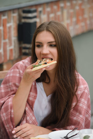 Funny brunette girl in a white blouse eating pizza at restaurant. Outdoorsの写真素材