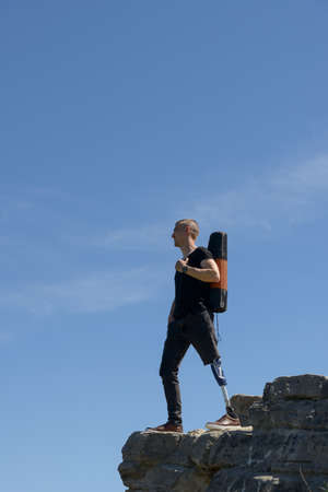 a man on a prosthetic leg travels the mountains. Dressed in black jeans and a T-shirt, he carrying matの写真素材