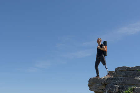 a man on a prosthetic leg travels the mountains. Dressed in black jeans and a T-shirt, he carrying matの写真素材