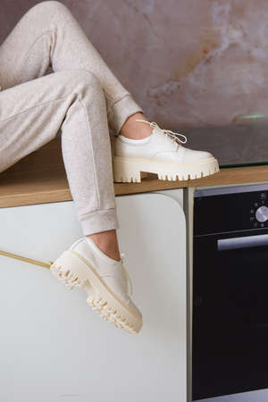 Part photo of a women in beige sports suit and stylish leather oxfords shoes posing on the kitchen. selective focusの写真素材