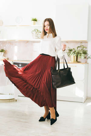 Portrait of fashionable women in a red skirt, white blouse and stylish suedeshoes with a buckle posing on the kitchenの写真素材