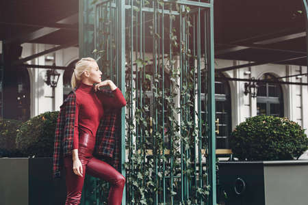 fashionable blonde girl with a red lipstick posing outdoors . Dressed in a red leather leggings, turtleneck and checkered jacket. fit figureの写真素材
