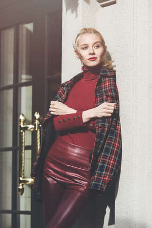 fashionable blonde girl with a red lipstick posing outdoors . Dressed in a red leather leggings, turtleneck and checkered jacket. fit figureの写真素材