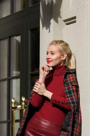 fashionable blonde girl with a red lipstick posing outdoors . Dressed in a red leather leggings,...