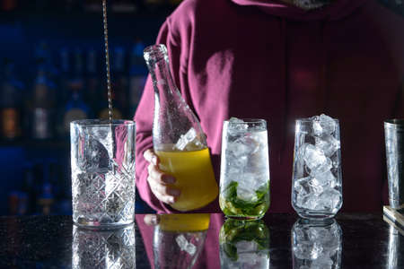 bartender making summer alcoholic cocktails mojito with rum, mint, lime and ice, bar tools, gray...
