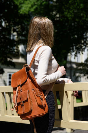 photo of a woman with a orange leather backpack with antique and retro look. Outdoors photo