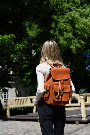 photo of a woman with a orange leather backpack with antique and retro look. Outdoors photo