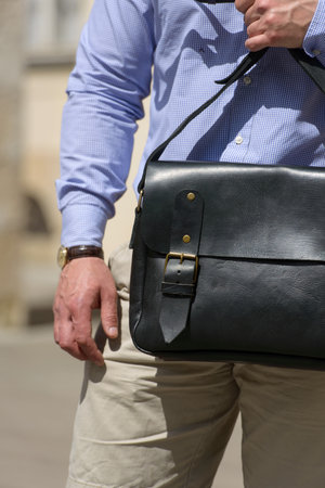 Part photo of a man with a black leather briefcase with antique and retro look. Outdoors photo