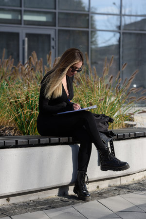 a woman fills out a questionnaire while sitting on a bench on the streetの写真素材