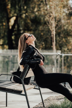 Fashionable young woman with long hair wearing solid long sleeve bodycon jumpsuits posing in a black leather jacket and sunglassesの写真素材