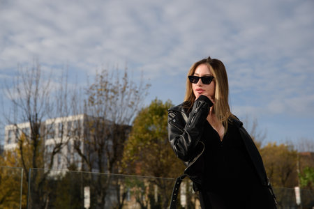 Fashionable young woman with long hair wearing solid long sleeve bodycon jumpsuits posing in a black leather jacket and sunglassesの写真素材