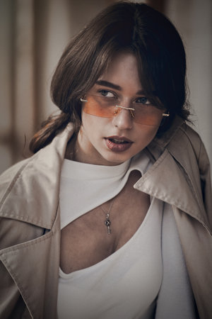 beautiful brunette girl in a sunglasses dressed in white blouse and beige coat. Stylish trendy...