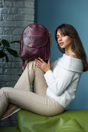 beautiful slender girl in beige pants and olive sweater posing with a small violet leather backpackの写真素材