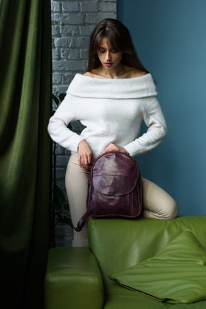 beautiful slender girl in beige pants and olive sweater posing with a small violet leather backpackの写真素材