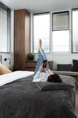 Woman with a phone on a bed in modern apartmentの写真素材