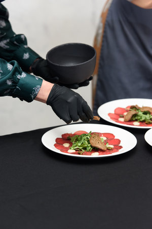 white dish with carpaccio of beef. the chef is preparing to serve a meal in a restaurant