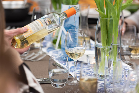 Waiter pouring white wine in a glass at a restaurant tableの写真素材