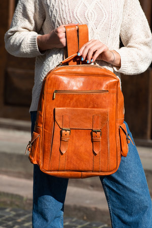 Part photo of a woman with a orange leather backpack with antique and retro look. Outdoors photoの写真素材