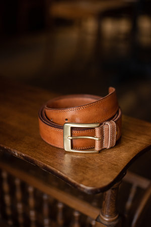 Brown leather belt with golden buckle on a wooden surfaceの写真素材