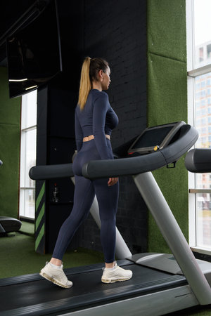 Beautiful muscular woman walking on a treadmill. wearing blue leggins and long sleeve topの写真素材