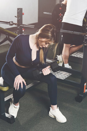 Woman doing biceps curl with dumbbells in seated position. wearing blue leggins and long sleeve top.の写真素材