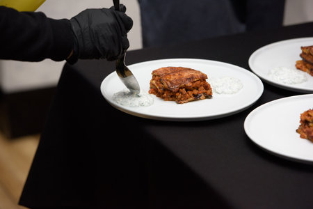 the chef in the restaurant preparing traditional greek moussaka in white plate on black tablecloth backgroundの写真素材