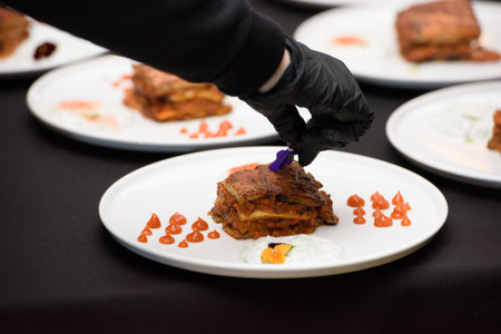 the chef in the restaurant preparing traditional greek moussaka in white plate on black tablecloth backgroundの写真素材