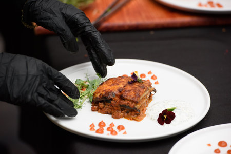the chef in the restaurant preparing traditional greek moussaka in white plate on black tablecloth backgroundの写真素材