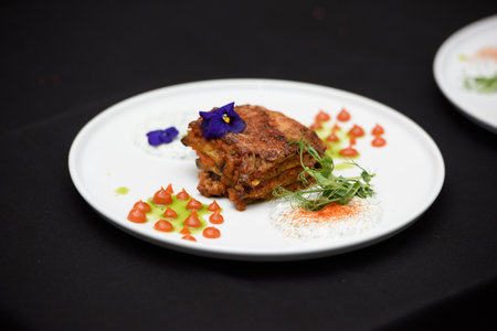 the chef in the restaurant preparing traditional greek moussaka in white plate on black tablecloth backgroundの写真素材