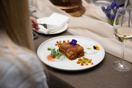 portion of traditional greek moussaka in white plate on a table in a restaurantの写真素材