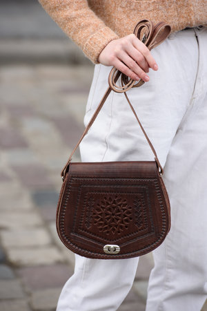 woman in white pants and a beige sweater poses outside with a small leather handbagの写真素材