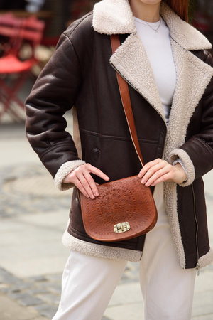 woman in white pants and a beige sweater poses outside with a small leather handbagの写真素材