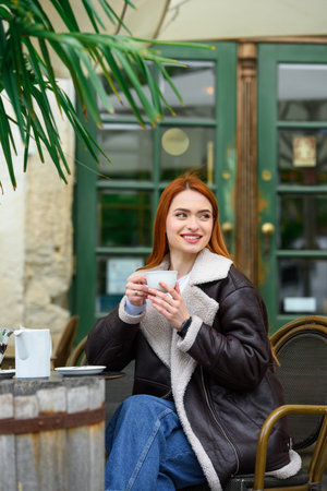 a red-haired girl in a leather jacket. cheerful woman with long red hair sits in a cafeの写真素材