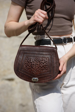 woman posing with a small brown leather bag with a carved pattern.の写真素材