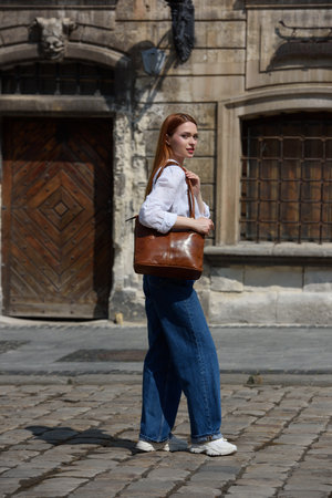 photo of a woman wearing blue jeans and white blouse with a brown leather handbag .の写真素材