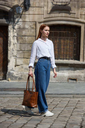 photo of a woman wearing blue jeans and white blouse with a brown leather handbag .の写真素材