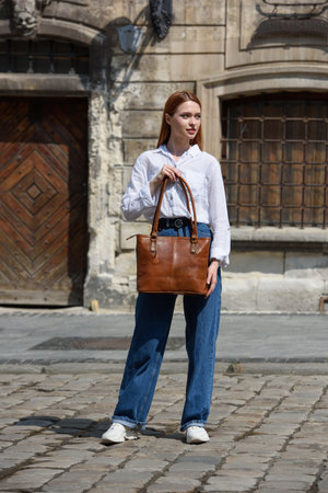 photo of a woman wearing blue jeans and white blouse with a brown leather handbag .の写真素材