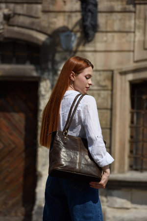 photo of a woman wearing blue jeans and white blouse with a brown leather handbag .の写真素材