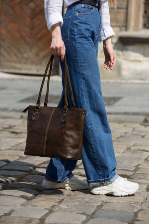 photo of a woman wearing blue jeans and white blouse with a brown leather handbag .の写真素材