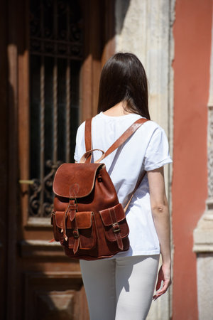 beautiful brunette girl in white leggings and T-shirt posing with a light brown leather backpack.の写真素材