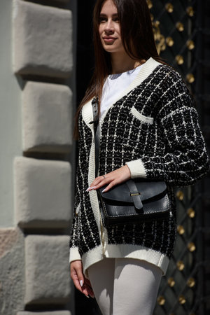 photo of beautiful woman in a white leggings, T-shirt and sweater posing with small black leather bagの写真素材
