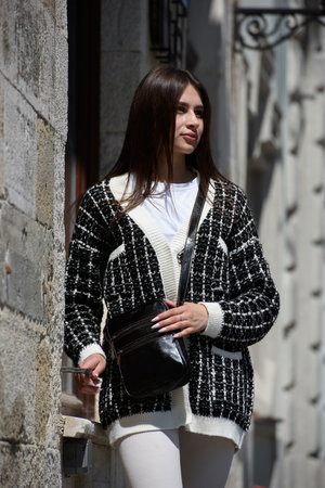 photo of beautiful woman in a white leggings, T-shirt and sweater posing with small black leather bagの写真素材